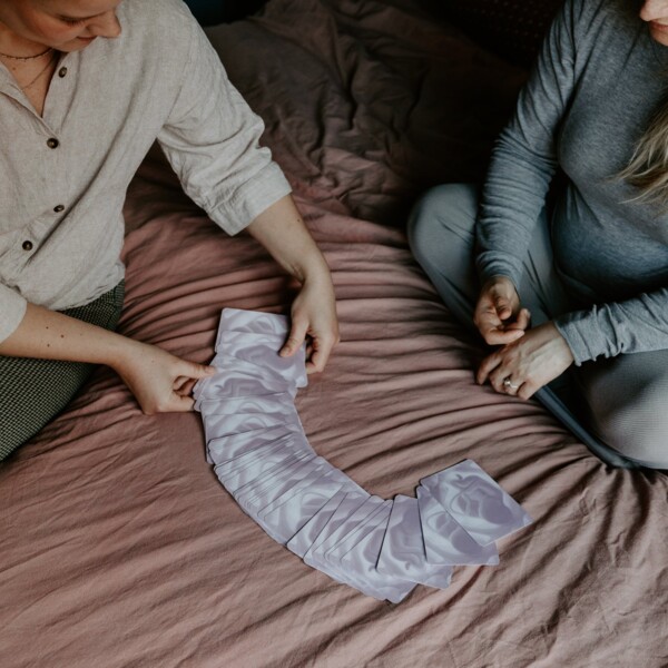 De behandelaar en zwangere vrouw zitten op bed terwijl de behandelaar affirmatiekaarten neerlegt.